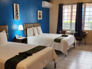 Bedroom with blue and tan walls, tile flooring, two double beds with white bedding, and sitting area