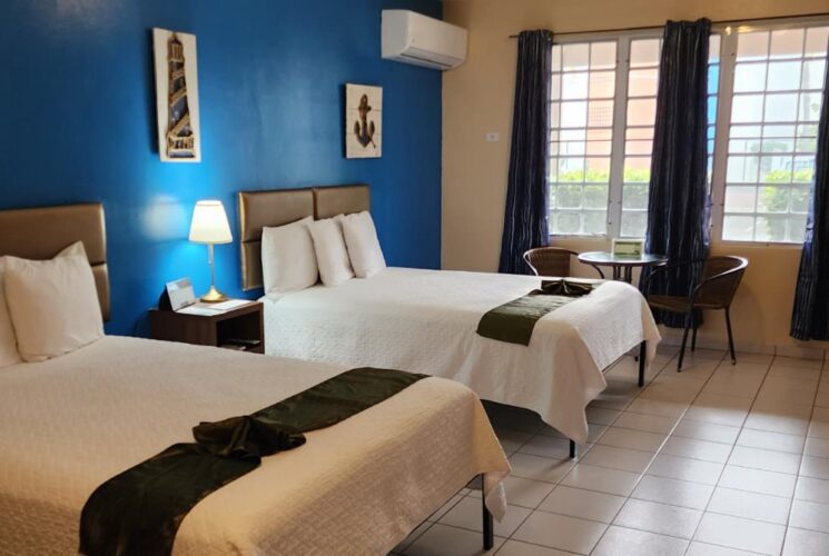 Bedroom with blue and tan walls, tile flooring, two double beds with white bedding, and sitting area