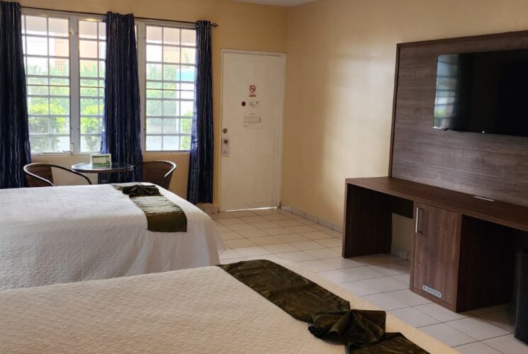 Bedroom with blue and tan walls, tile flooring, two double beds with white bedding, sitting area, flatscreen TV, and mini fridge