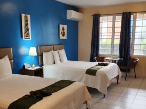 Bedroom with blue and tan walls, tile flooring, two queen beds with white bedding, and sitting area