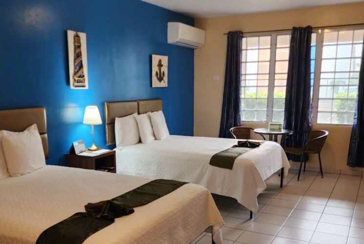 Bedroom with blue and tan walls, tile flooring, two queen beds with white bedding, and sitting area