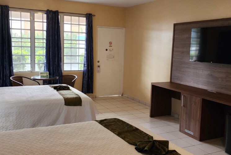 Bedroom with blue and tan walls, tile flooring, two queen beds with white bedding, sitting area, flatscreen TV, and mini fridge