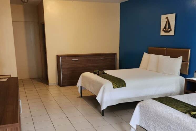 Bedroom with blue and tan walls, tile flooring, two queen beds with white bedding, flatscreen TV and dark wooden furniture