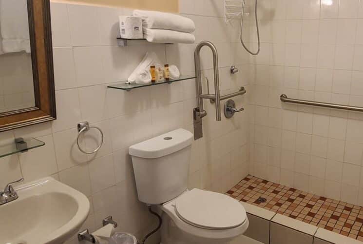 Bathroom with stand up shower, white tile, white toilet, white pedestal sink, and framed mirror