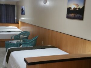 Bedroom with white walls with light brown wood paneling, tile flooring, two beds with white bedding, and sitting area