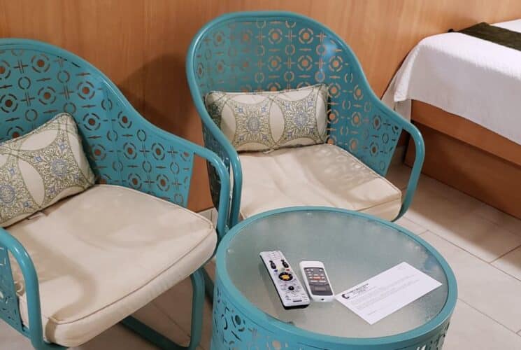 Bedroom's sitting area with turquoise metal chairs with white cushions and small turquoise metal circular table with frosted glass top