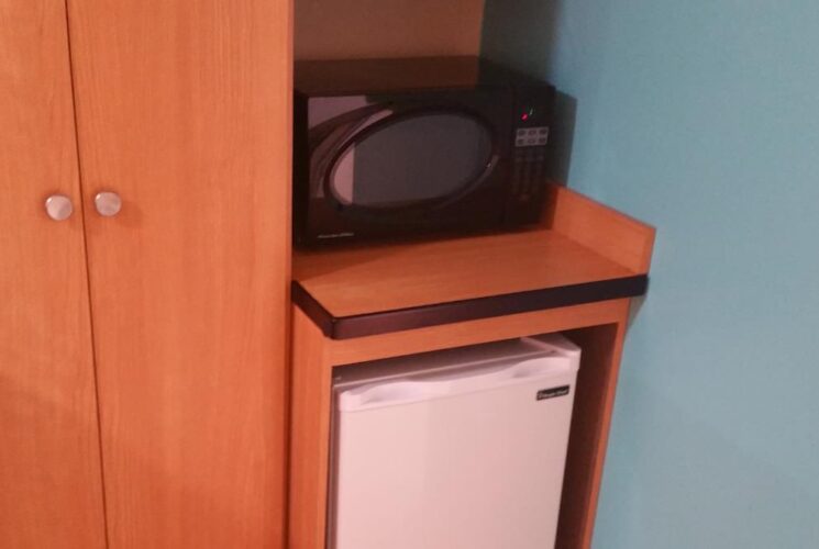 Bedroom with blue and tan walls, light wooden armoire, mini fridge, and microwave