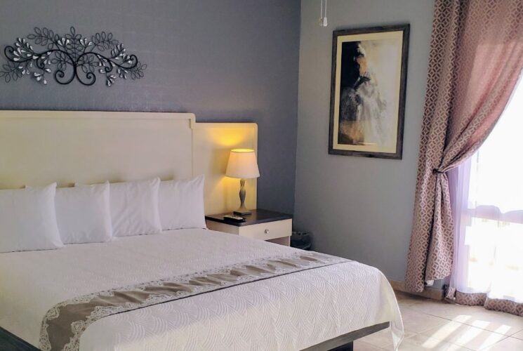 Bedroom with light blue walls, tile flooring, king bed with white bedding, and double door with mauve and white curtains