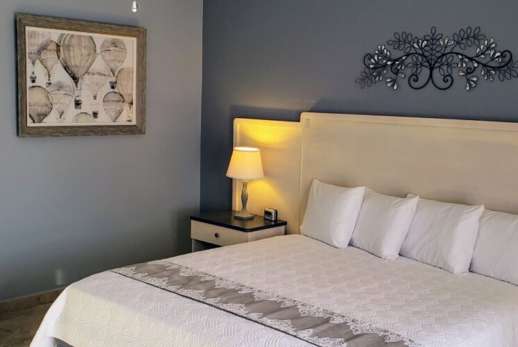 Bedroom with light blue walls, tile flooring, king bed with white bedding, and white dresser with mirror