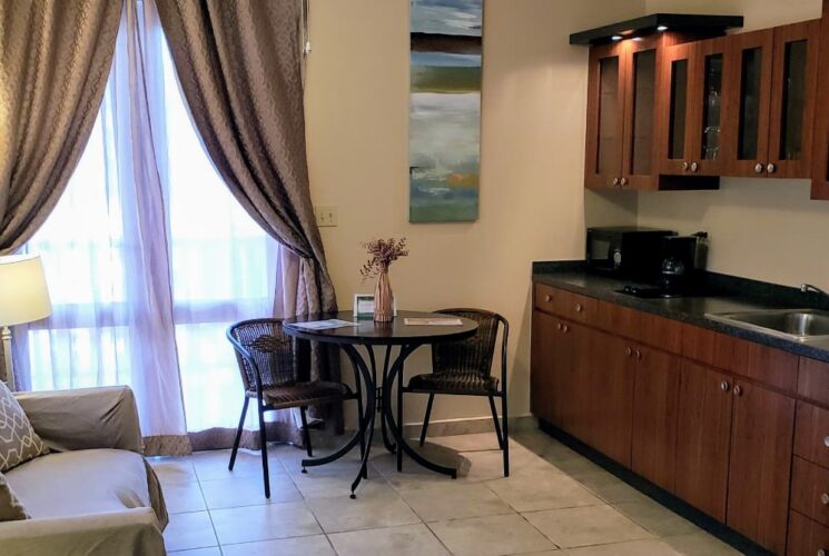 Bedroom suite with tan walls, tile flooring, small sofa, table with chairs, and full kitchen