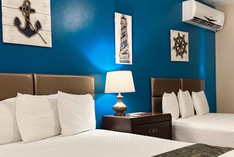 Bedroom with blue and tan walls, tile flooring, two queen beds with white bedding, and dark wooden nightstand