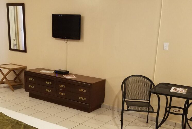 Bedroom with tan walls, tile flooring, two queen beds with white bedding, sitting area, and flatscreen TV