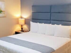 Bedroom with light blue and tan walls, tile flooring, blue upholstered headboard, and white bedding