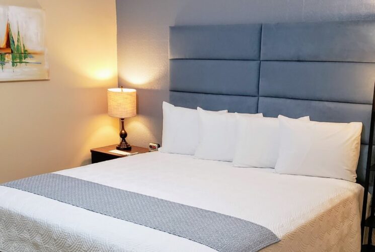 Bedroom with light blue and tan walls, tile flooring, blue upholstered headboard, and white bedding