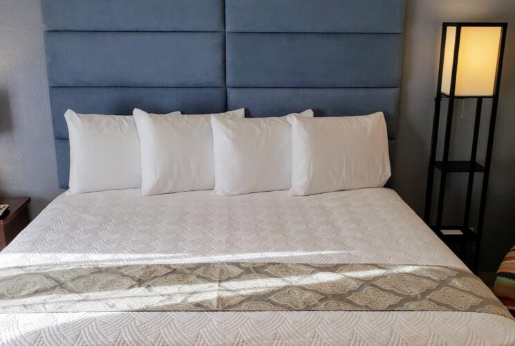 Bedroom with light blue and tan walls, tile flooring, blue upholstered headboard, white bedding, and multicolored chair