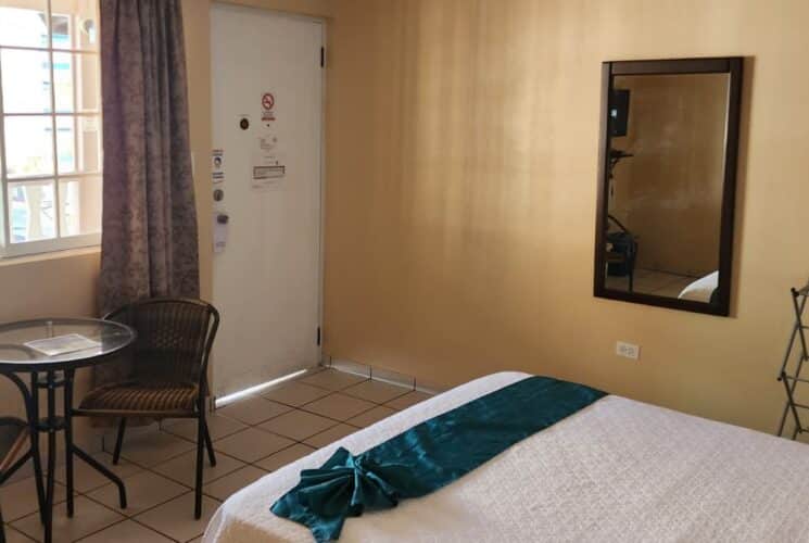 Bedroom with tan walls, tile flooring, dark wooden furniture, white bedding, and sitting area