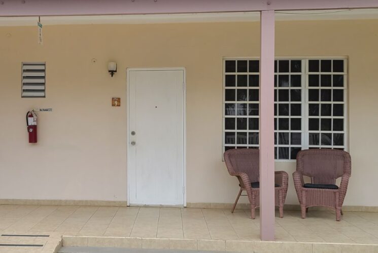 Exterior view of property painted tan with tiled room entries, white doors, mauve wicker patio chairs, and mauve awning posts