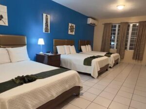 Bedroom with blue and tan walls, tile flooring, three beds with white bedding, flatscreen TV, and mini fridge