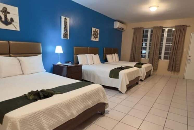 Bedroom with blue and tan walls, tile flooring, three beds with white bedding, flatscreen TV, and mini fridge