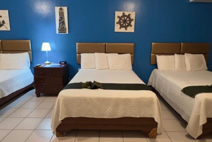Bedroom with blue and tan walls, tile flooring, three beds with white bedding, and dark wooden nightstand