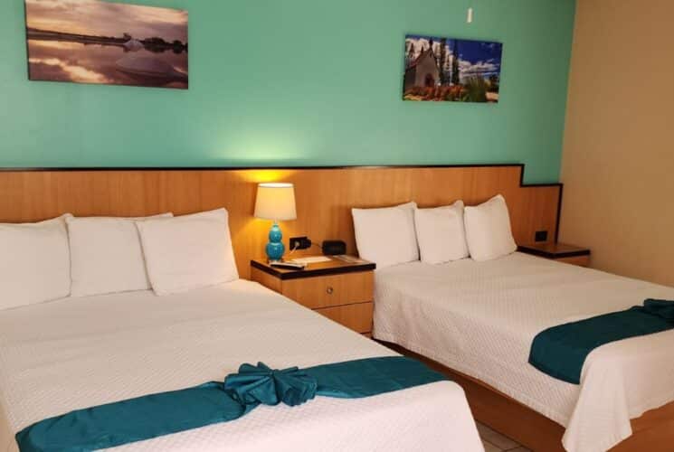 Large suite with light green and tan walls, tile flooring, and two queen beds with white bedding