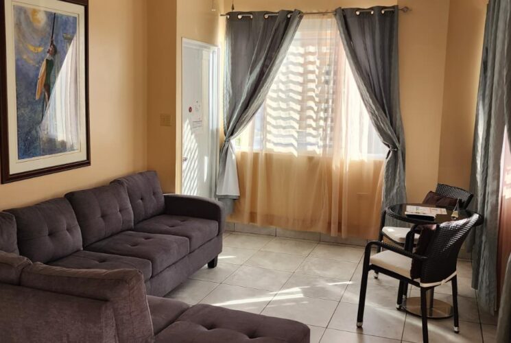 Large suite with light tan walls, tile flooring, upholstered gray sectional sofa, sitting area, and flatscreen TV