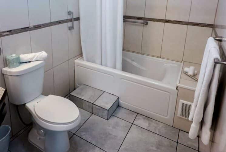 Bathroom with tub and shower, light colored tile, white toilet, white sink, and mirror