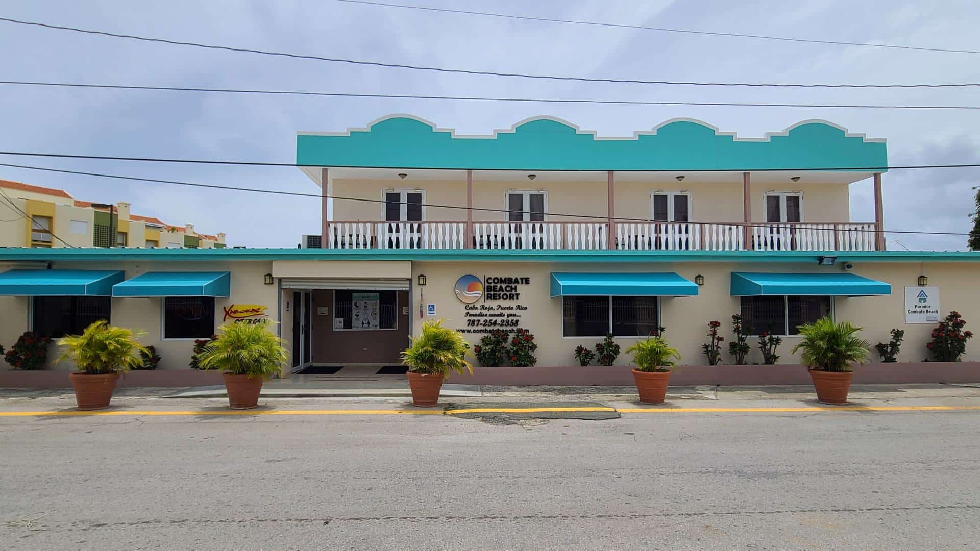 Exterior view of the property painted light cream with teal awnings and pops of light lavender with large fern-like potted plants