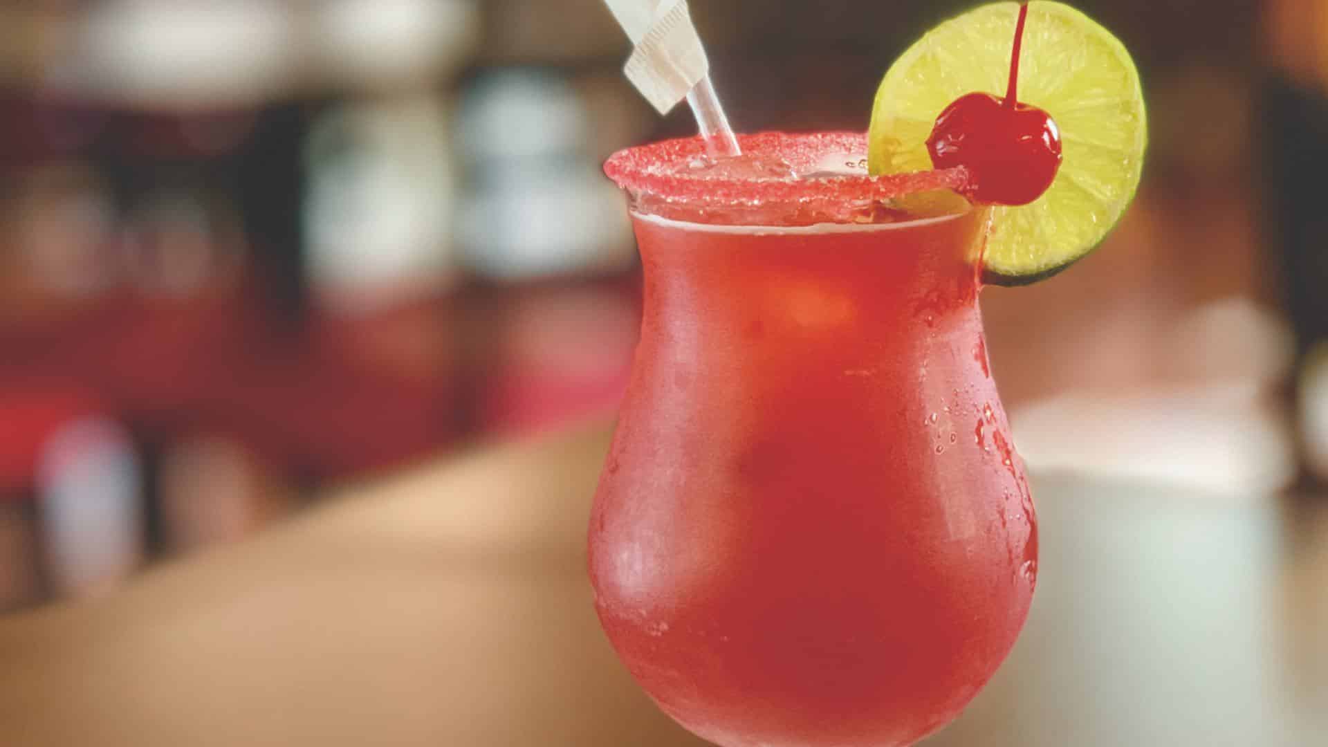 Close up view of red alcoholic drink in glass with slice of lime and maraschino cherry