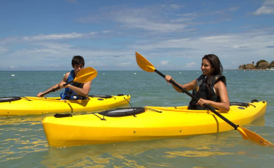 Dos personas en kayaks amarillos individuales remando en aguas azul verdosas